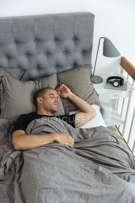 De cima de pacífico macho deitado em cama macia sob cobertor e dormindo de manhã no quarto — Fotografia de Stock