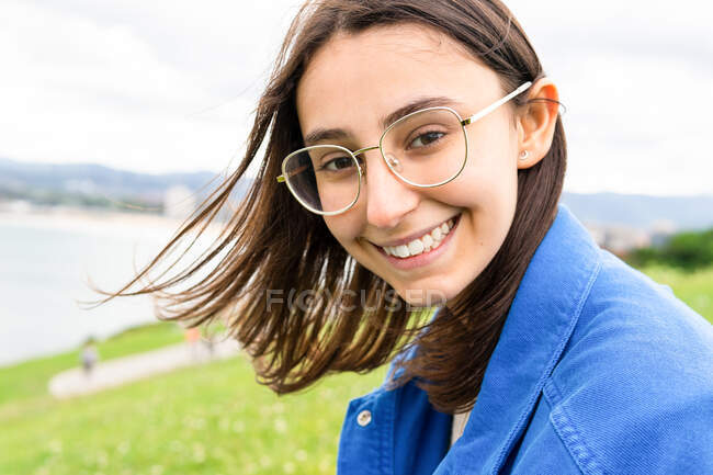 Delighted female with eyes closed sitting on green hill and enjoying view of sea on cloudy day — Stock Photo