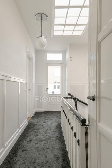 Vista panorámica del pasillo estrecho con escalera y paredes blancas en apartamento moderno con ventana del ático - foto de stock
