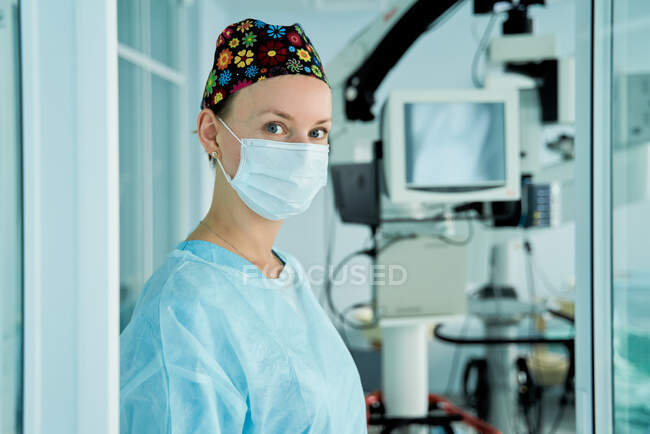 Allegro medico femminile adulto in maschera sterile e cappuccio ornamentale guardando la fotocamera in ospedale — Foto stock