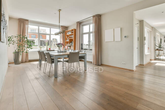 Modern home interior of spacious dining area with table and chairs in front of large window in open space apartment with white walls and wooden floor — Stock Photo