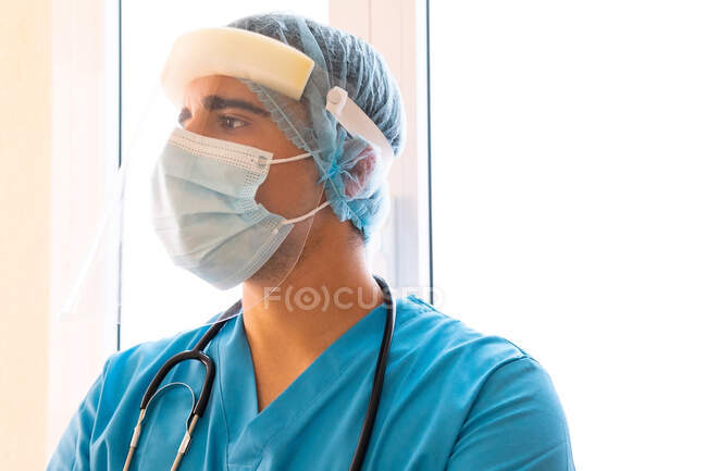 Médecin masculin avec écran protecteur en plastique tout en travaillant à la clinique et en regardant ailleurs — Photo de stock