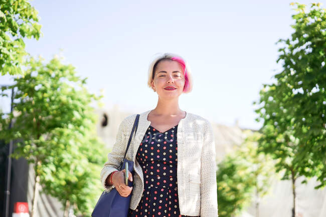 Восхитительная альтернативная женщина с окрашенными волосами, стоящая на улице в солнечный день летом и смотрящая в камеру — стоковое фото
