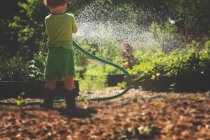 Маленький мальчик поливает растения в саду — стоковое фото