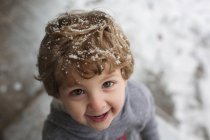 Улыбающийся маленький мальчик со снегом в волосах — стоковое фото