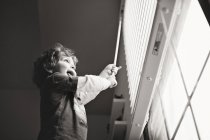 Счастливый маленький мальчик играет с жалюзи — стоковое фото