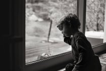 Симпатичный маленький мальчик сидит у окна — стоковое фото