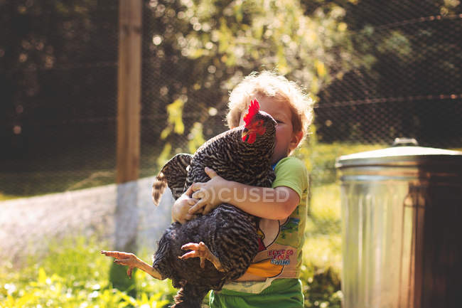 Pequeño niño abrazando gran gallina - foto de stock
