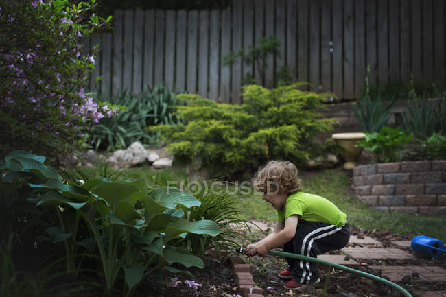 Pequeno menino regando plantas no jardim — Fotografia de Stock