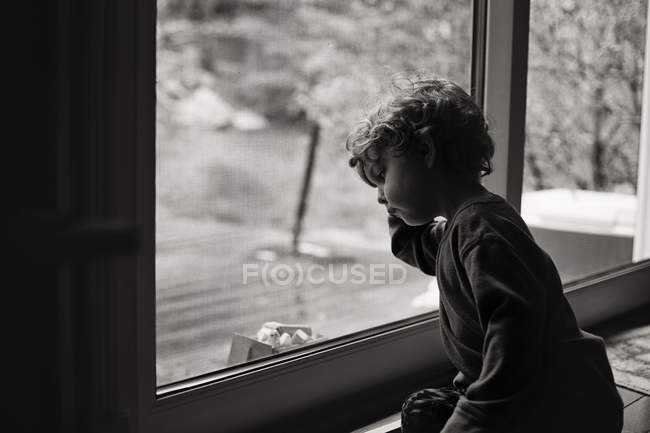 Mignon petit garçon assis près de la fenêtre — Photo de stock