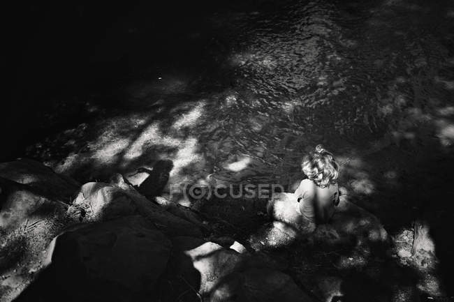 Menino sentado em pedra perto do rio — Fotografia de Stock