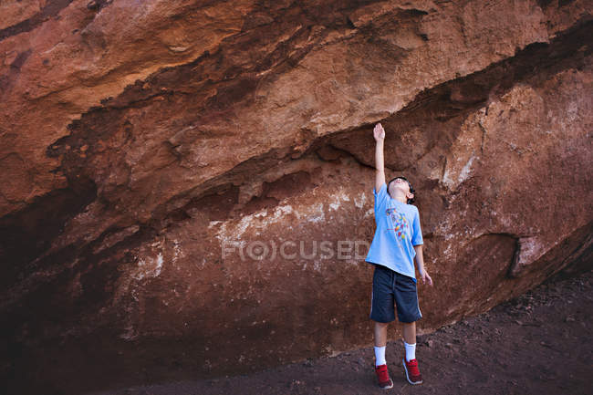 Маленький хлопчик стоїть біля величезної скелі — стокове фото