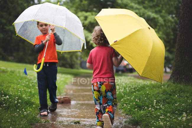Маленькие мальчики ходят с зонтиками — стоковое фото