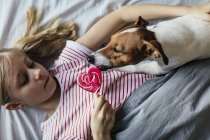 Girl eating pink lollipop near cute dog at home, selective focus — Stock Photo