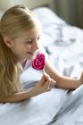 Дівчина використовує цифровий планшет і їсть рожевий льодяник вдома, фокус на передньому плані — стокове фото