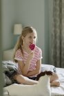 Girl eating pink lollipop on bed, selective focus — Stock Photo