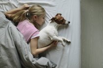 Vista elevada de chica con lindo perro en la cama - foto de stock