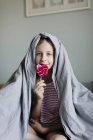 Menina comendo pirulito rosa na cama, foco seletivo — Fotografia de Stock