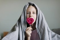 Дівчина їсть барвистий льодяник на ліжку, вибірковий фокус — стокове фото