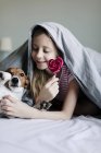 Fille manger sucette colorée avec chien sur le lit, mise au point sélective — Photo de stock