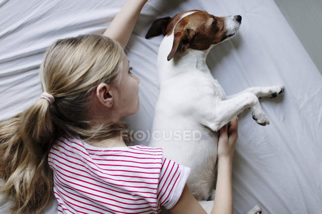 Vista elevada de chica con lindo perro en la cama - foto de stock