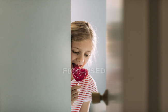 Chica comer caramelo piruleta en casa, enfoque selectivo - foto de stock
