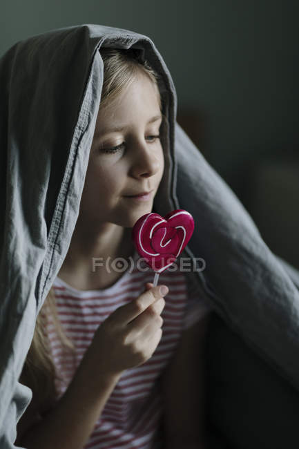 Дівчина їсть рожевий льодяник вдома, вибірковий фокус — стокове фото
