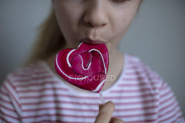 Vista recortada de niña comiendo piruleta rosa, enfoque selectivo - foto de stock