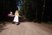 Menina andando com balões na estrada da floresta — Fotografia de Stock
