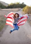 Chica saltando mientras sostiene la bandera americana - foto de stock