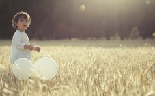 Boy holding balloons and standing in meadow — Stock Photo