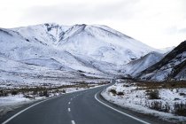 Пустая дорога с заснеженными горами — стоковое фото