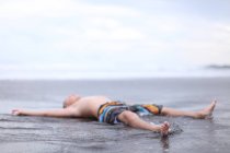 Niño acostado en la playa - foto de stock