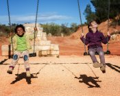 Smiling little children swinging — Stock Photo