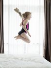 Menina no traje de natação pulando na cama — Fotografia de Stock