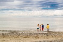 Вид сзади на четырех детей, стоящих на пляже — стоковое фото