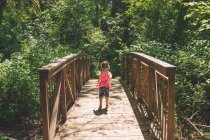 Young girl walking across bridge in woods — Stock Photo