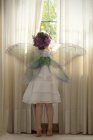 Girl wearing fairy costume looking out of window — Stock Photo