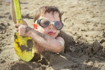 Niño enterrado en la arena en la playa - foto de stock