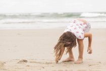 Маленькая девочка рисует на песке — стоковое фото