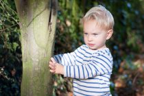 Niño de pie junto al árbol - foto de stock