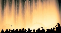 Силуэты людей перед освещенным фонтаном — стоковое фото