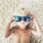 Toddler lying on floor wearing sunglasses — Stock Photo