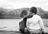 Sisters sitting on jetty by lake — Stock Photo