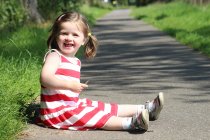 Girl sitting on footpath and smiling — Stock Photo