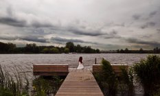 Mulher sentada no molhe pelo lago no verão — Fotografia de Stock
