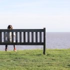 Mädchen sitzt auf Bank und blickt aufs Meer — Stockfoto