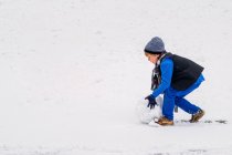 Мальчик катит снежный шар — стоковое фото