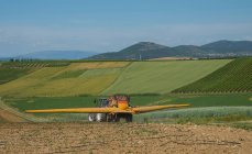 Tractor fertilizing field in valley — Stock Photo