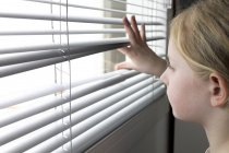 Girl looking through window blinds — Stock Photo
